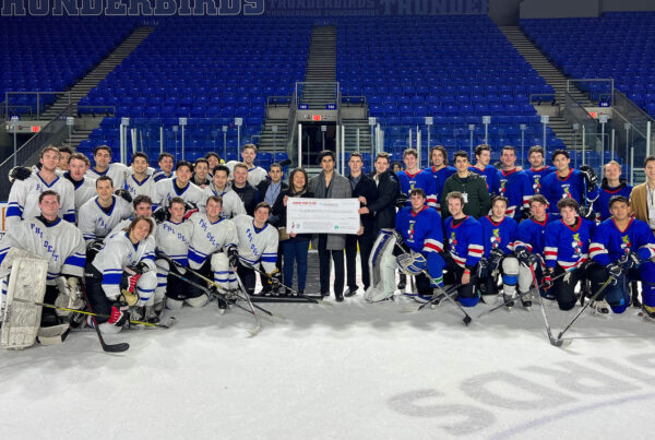 A group of players of Phi Delta Theta and Beta Theta Pi hold a large cheque at center ice.