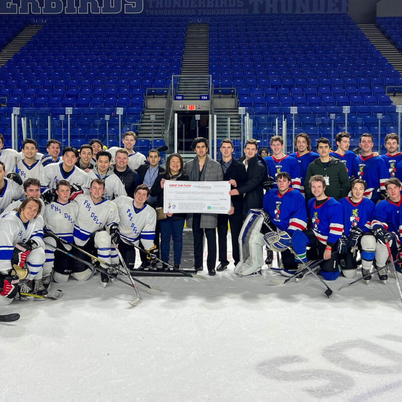 A group of players of Phi Delta Theta and Beta Theta Pi hold a large cheque at center ice.