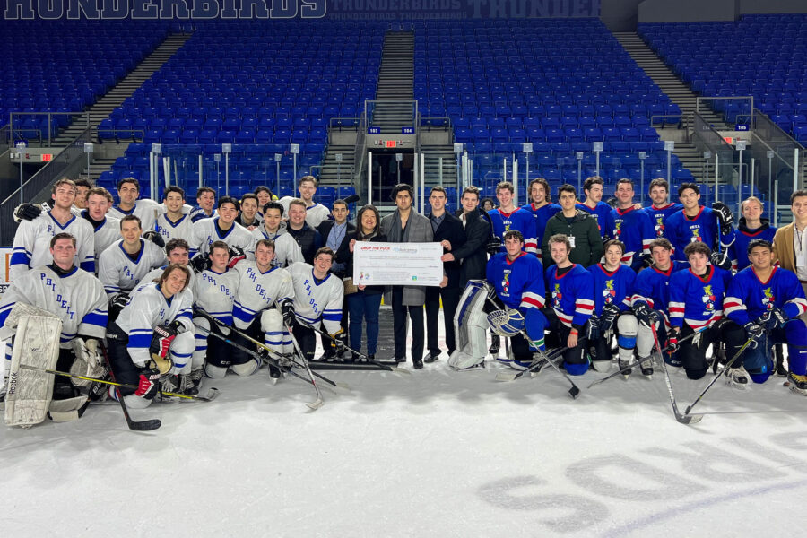 A group of players of Phi Delta Theta and Beta Theta Pi hold a large cheque at center ice.