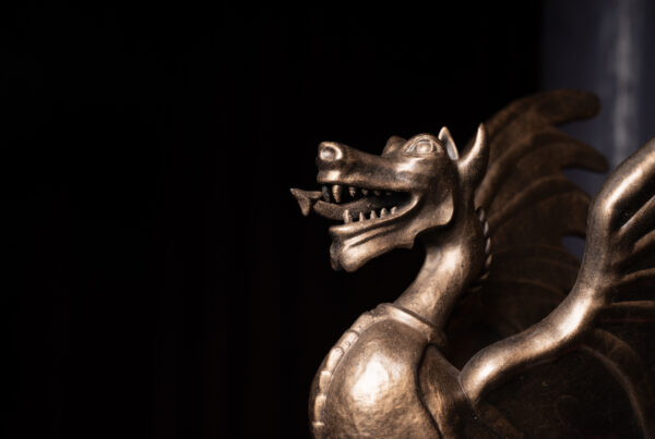A metallic dragon statue with open jaws and wings, set against a dark background.