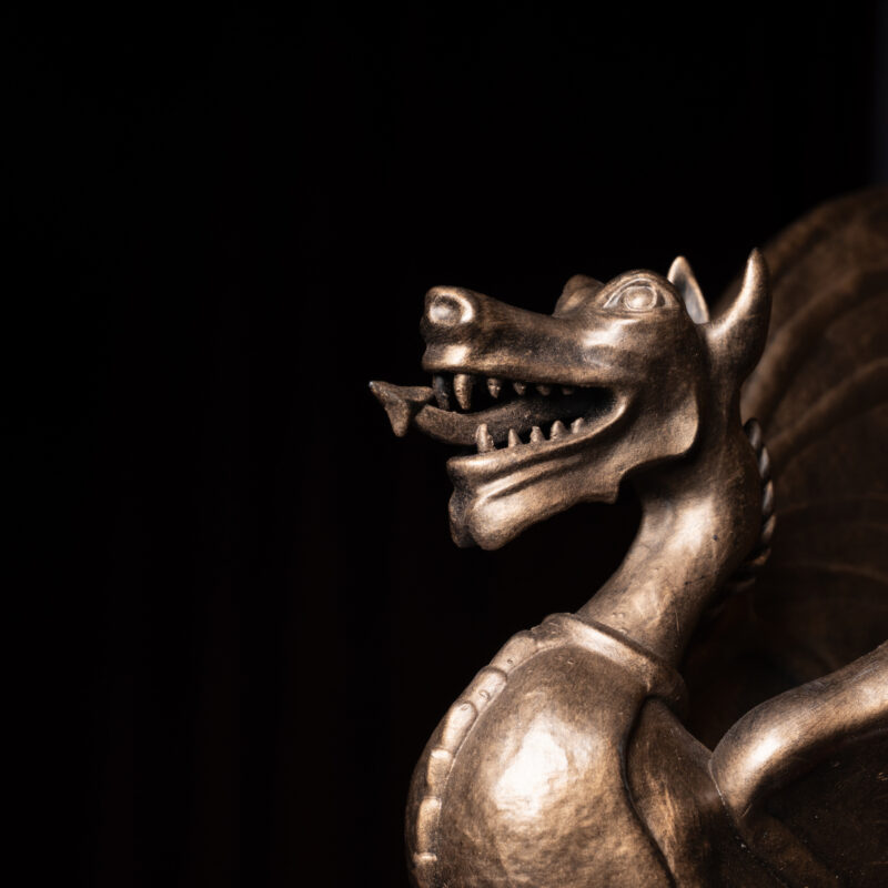 A metallic dragon statue with open jaws and wings, set against a dark background.